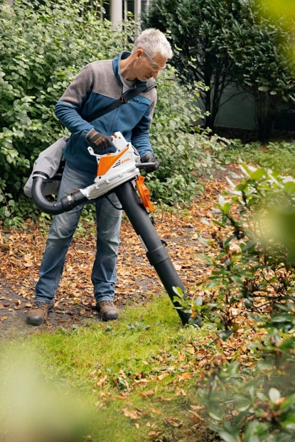 Un homme aspirant les feuilles de son jardin