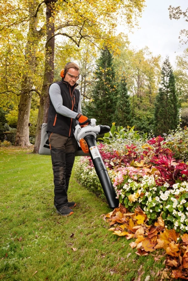 Un homme qui aspire les feuilles mortes dans le jardin